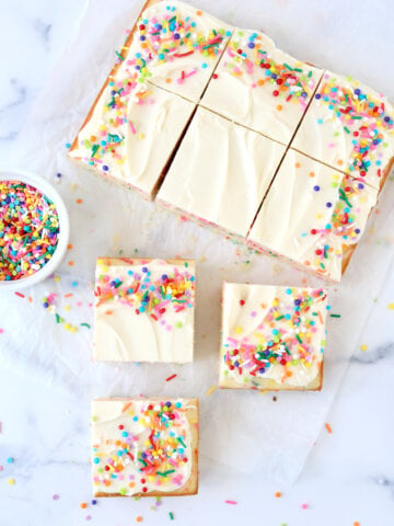 A square cake cut into nine pieces with rainbow sprinkles.