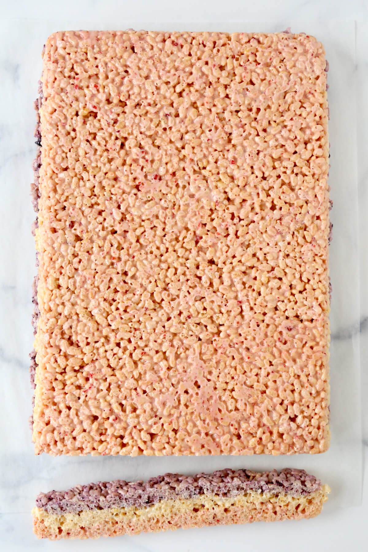 A sheet of pink rice krispie treats with a piece cut off.