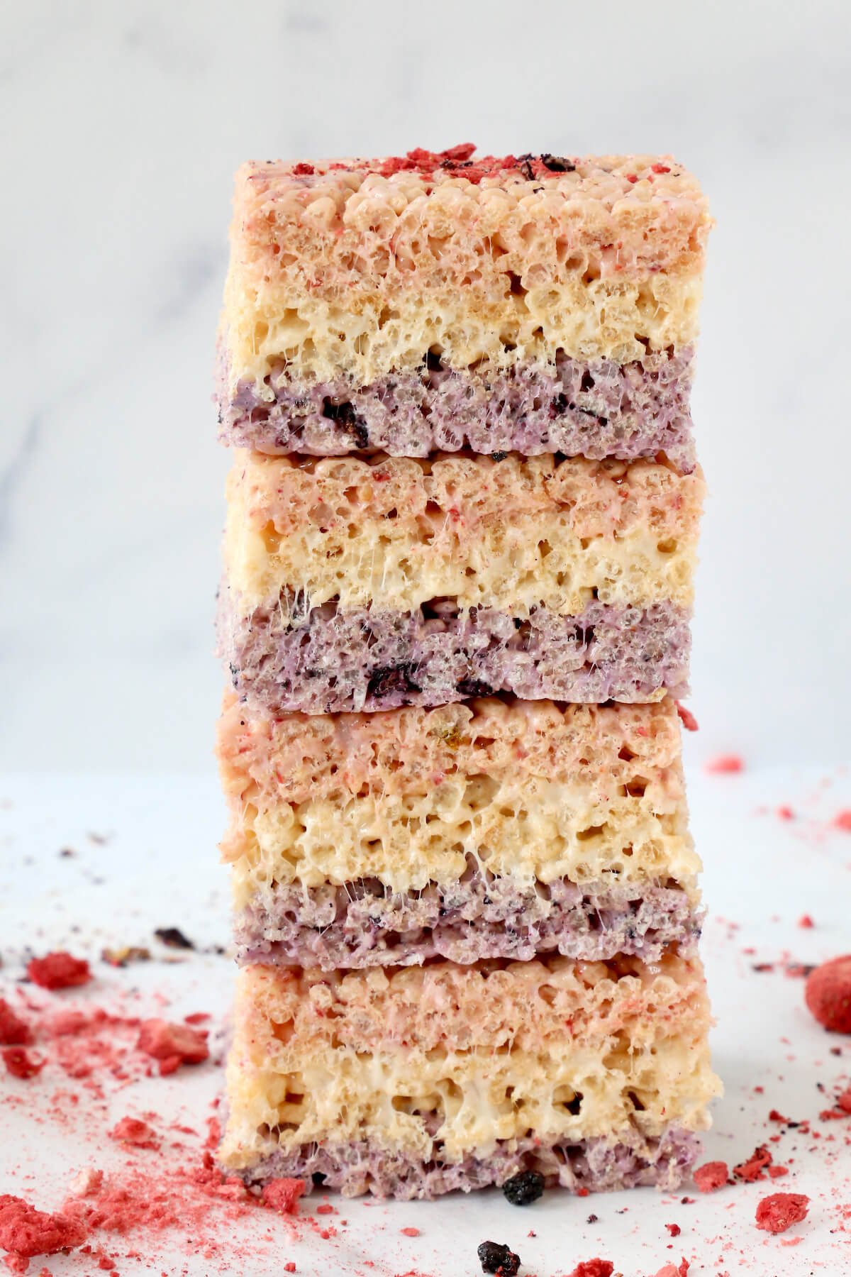 A stack of four rice krispie treats next to crumbled freeze dried strawberries.  