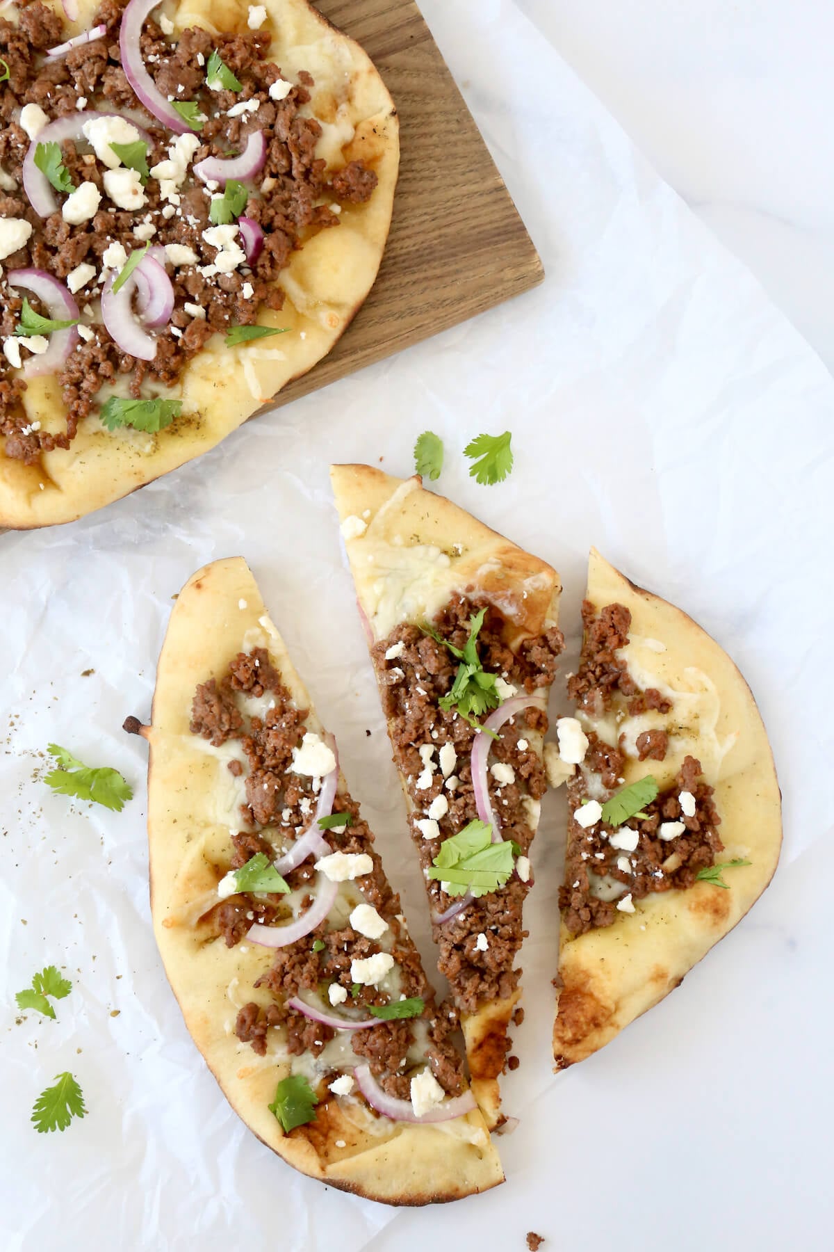 A flatbread pizza topped with lamb, feta cheese and cilantro cut into three slices.