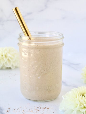 A glass jar filled with a light brown smooth and a gold metal straw.