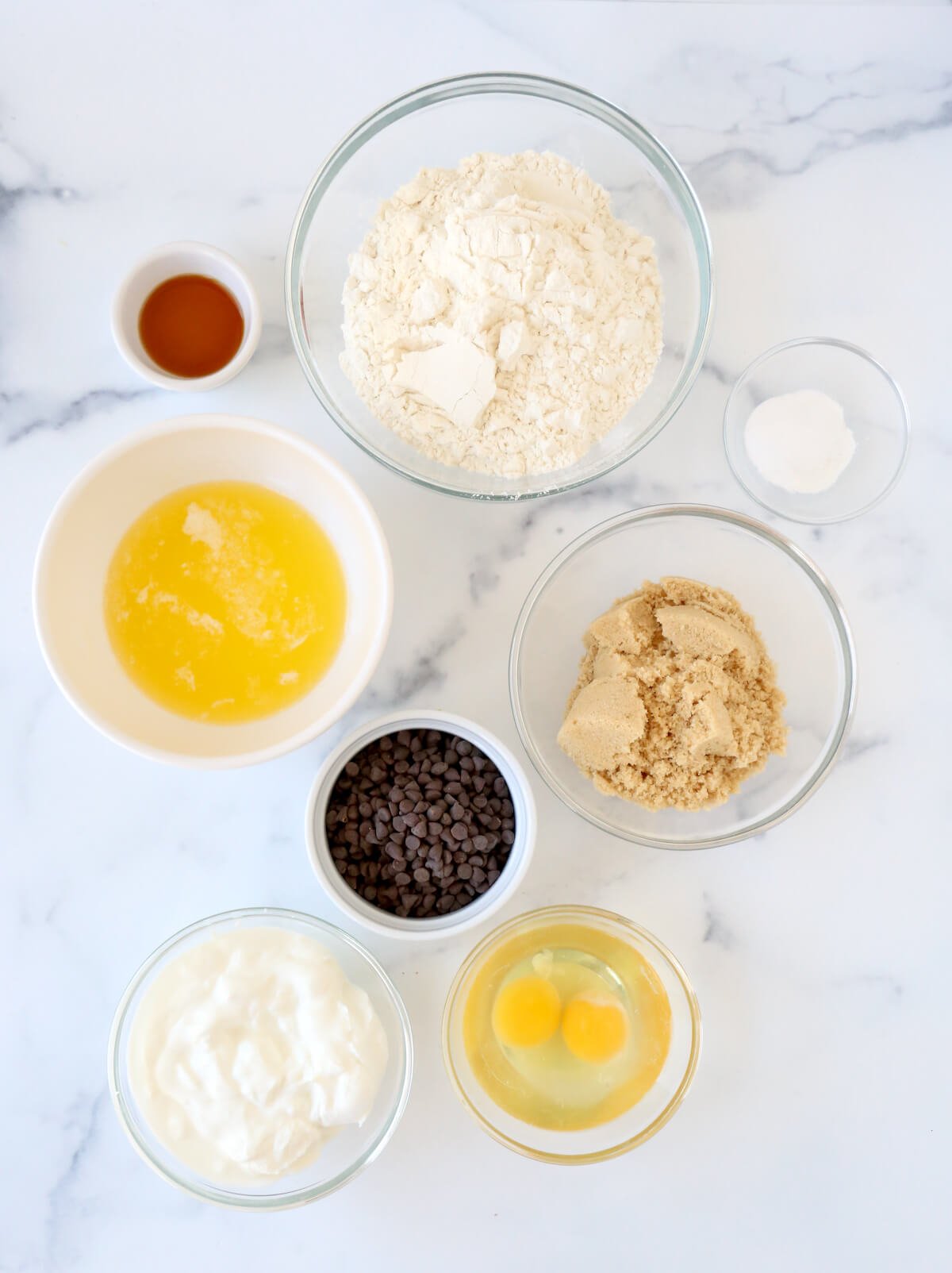 Bowls of flour, brown sugar, melted butter, eggs, sour cream and chocolate chips. 