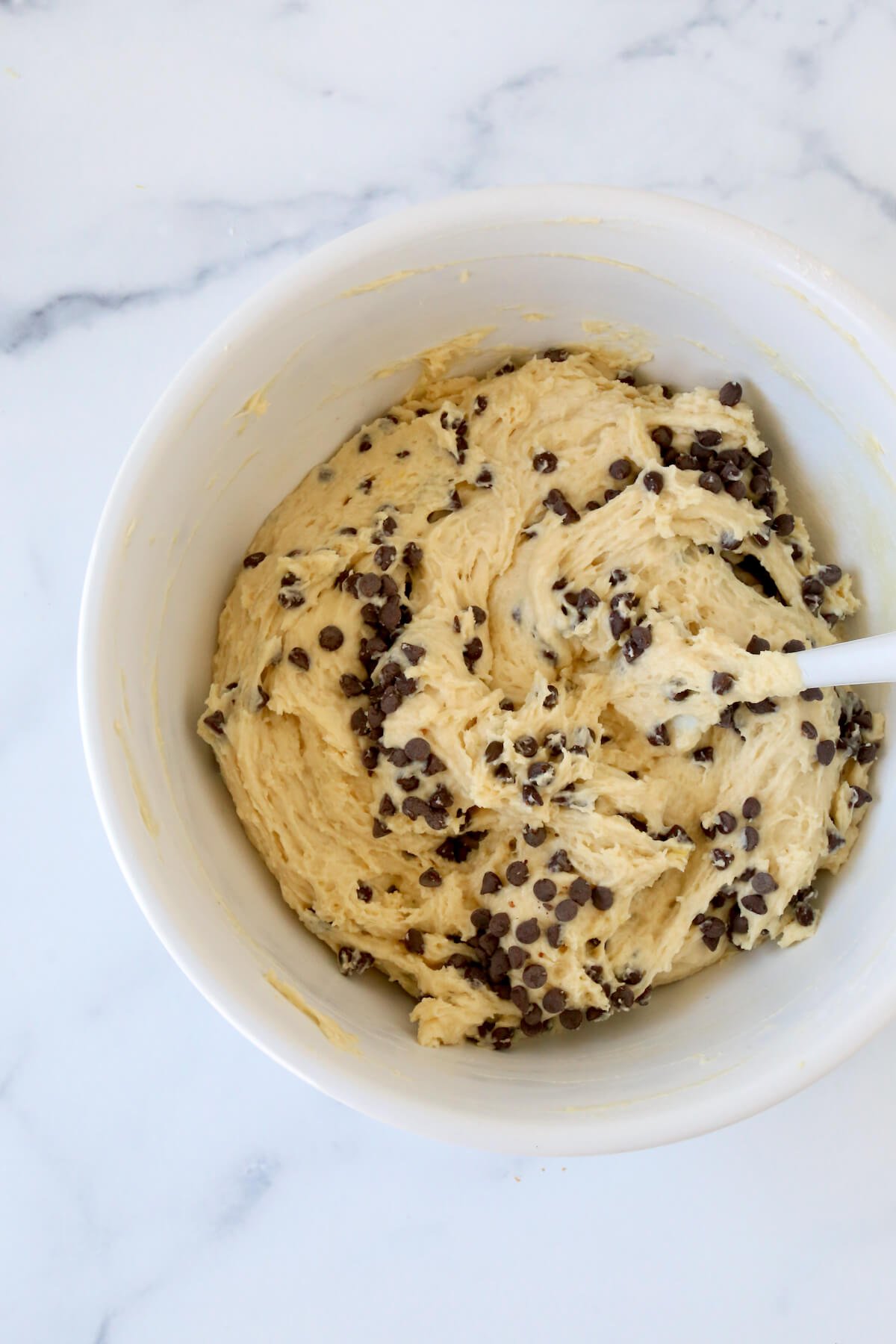 A white bowl filed with muffin batter with chocolate chips. 