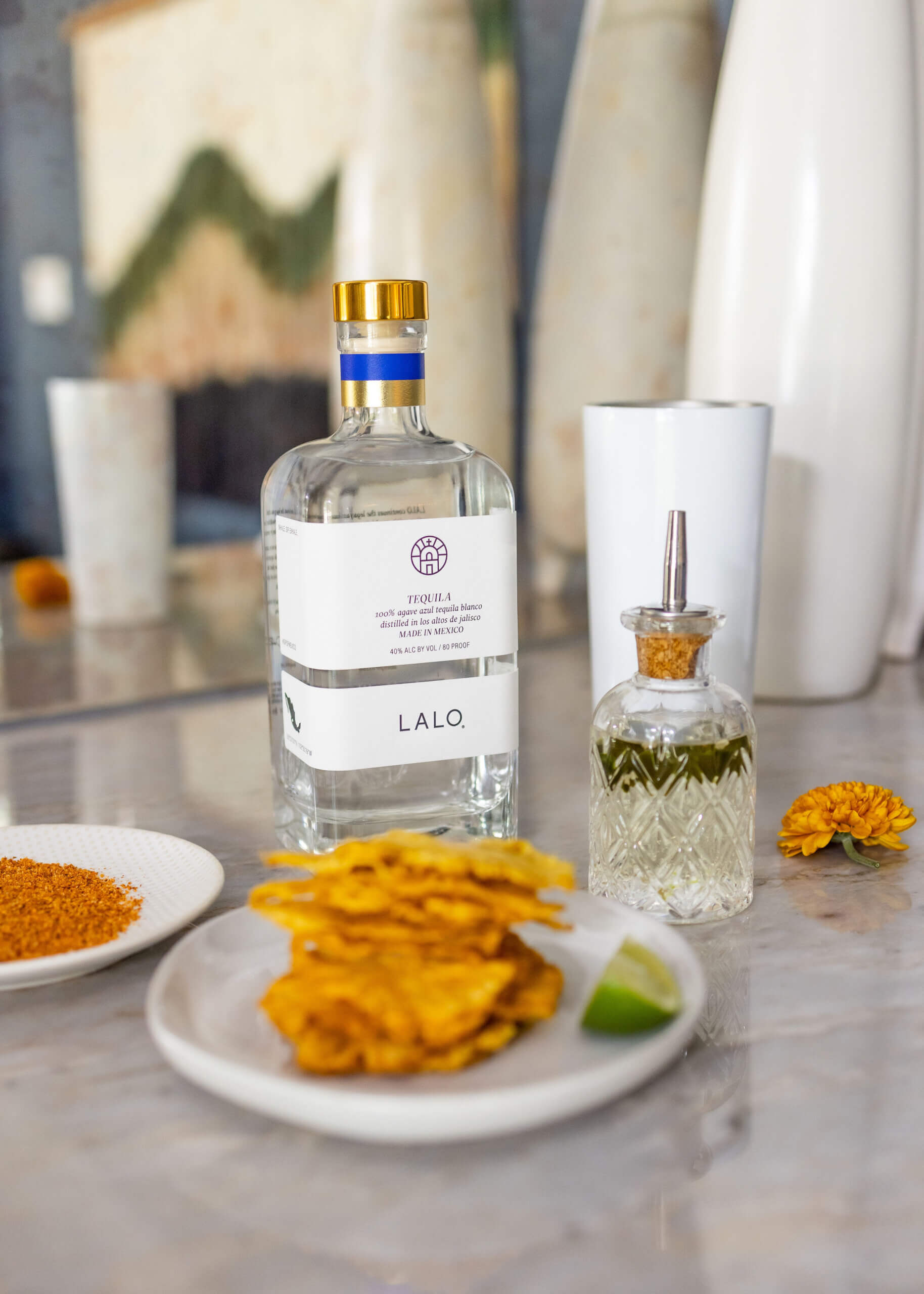A tequila bottle, a crystal bottle and a plate with dried pineapple with a lime slice.  