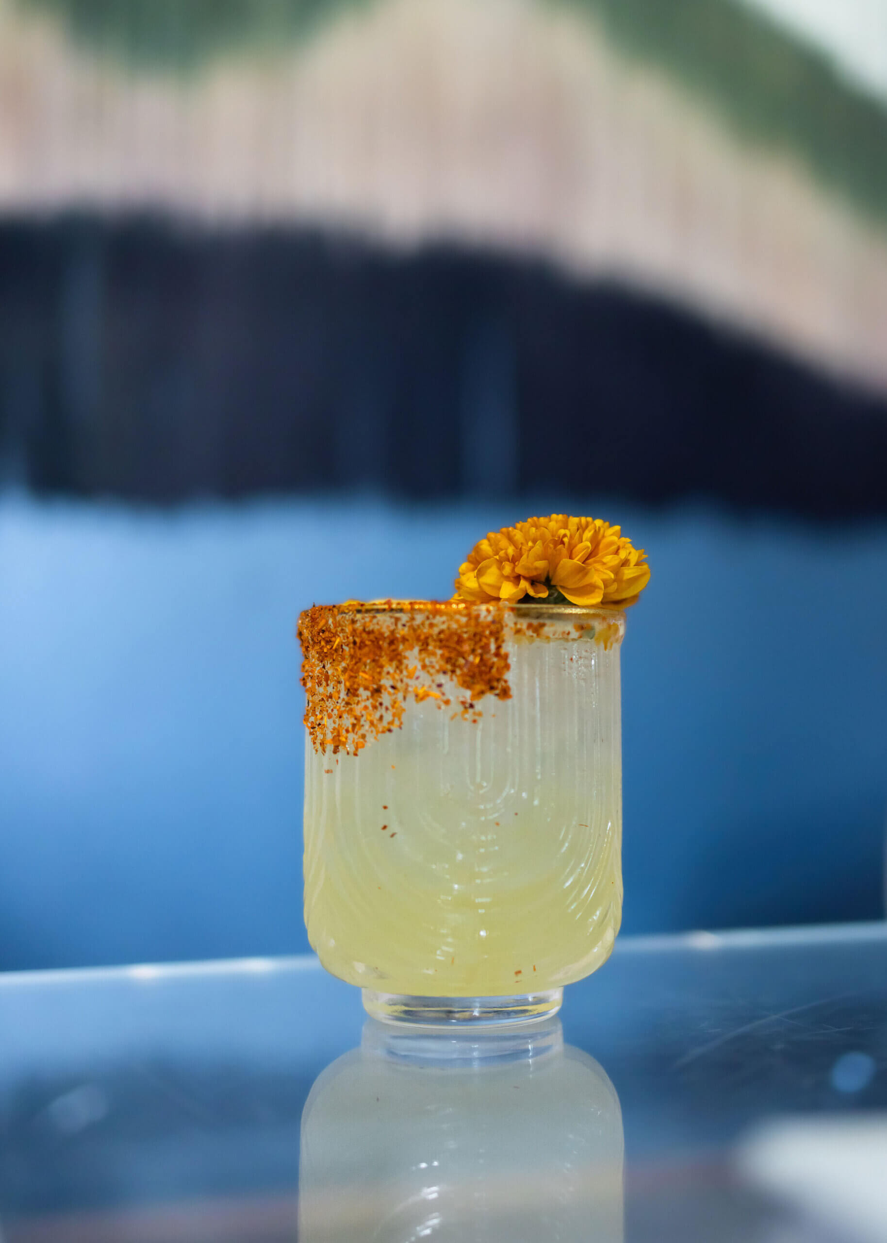 A glass with a yellow liquid inside, spicy salt on the rim and an orange flower on top.  