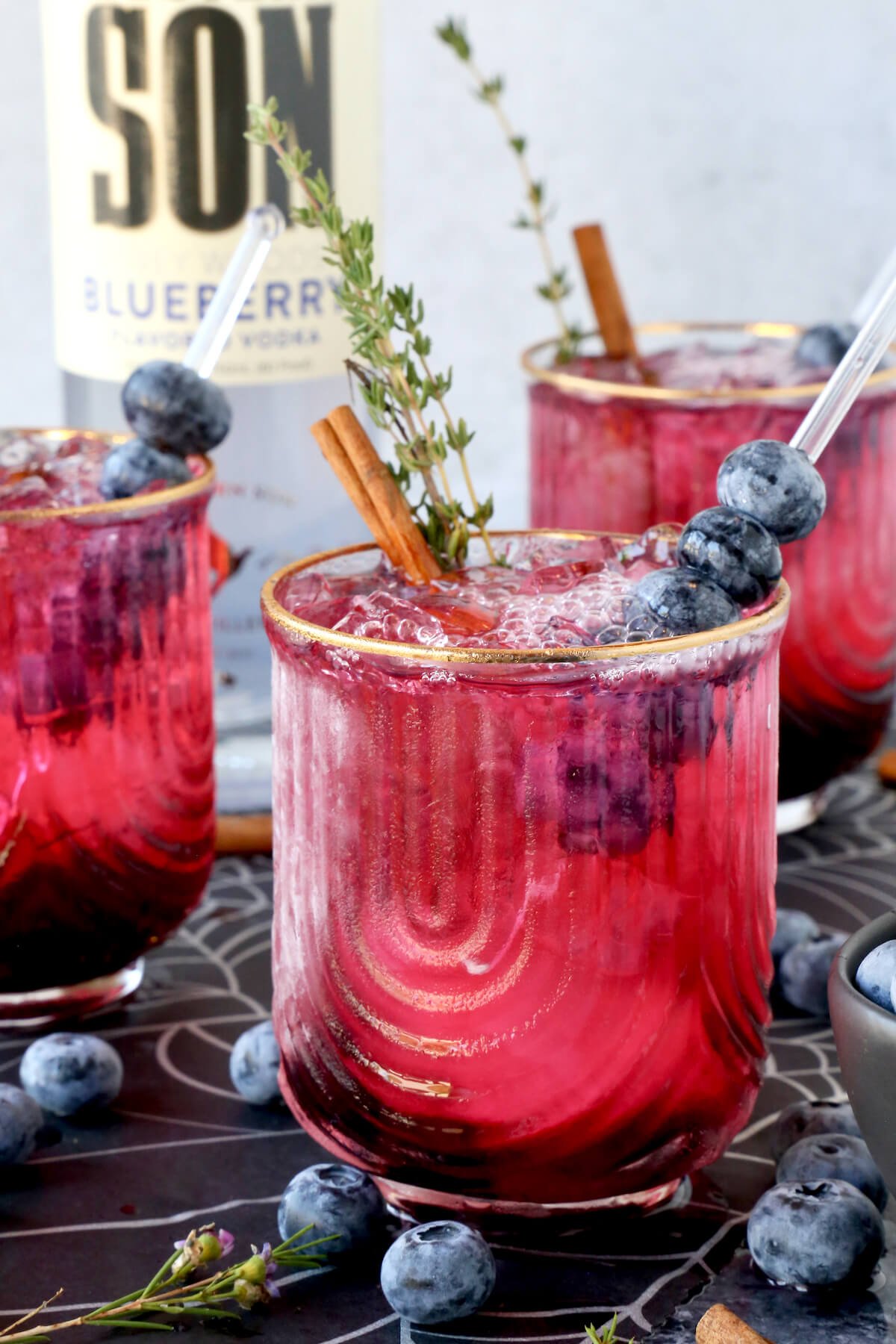 Three glasses filled with a pink drink with blueberries on top and smoke coming out.