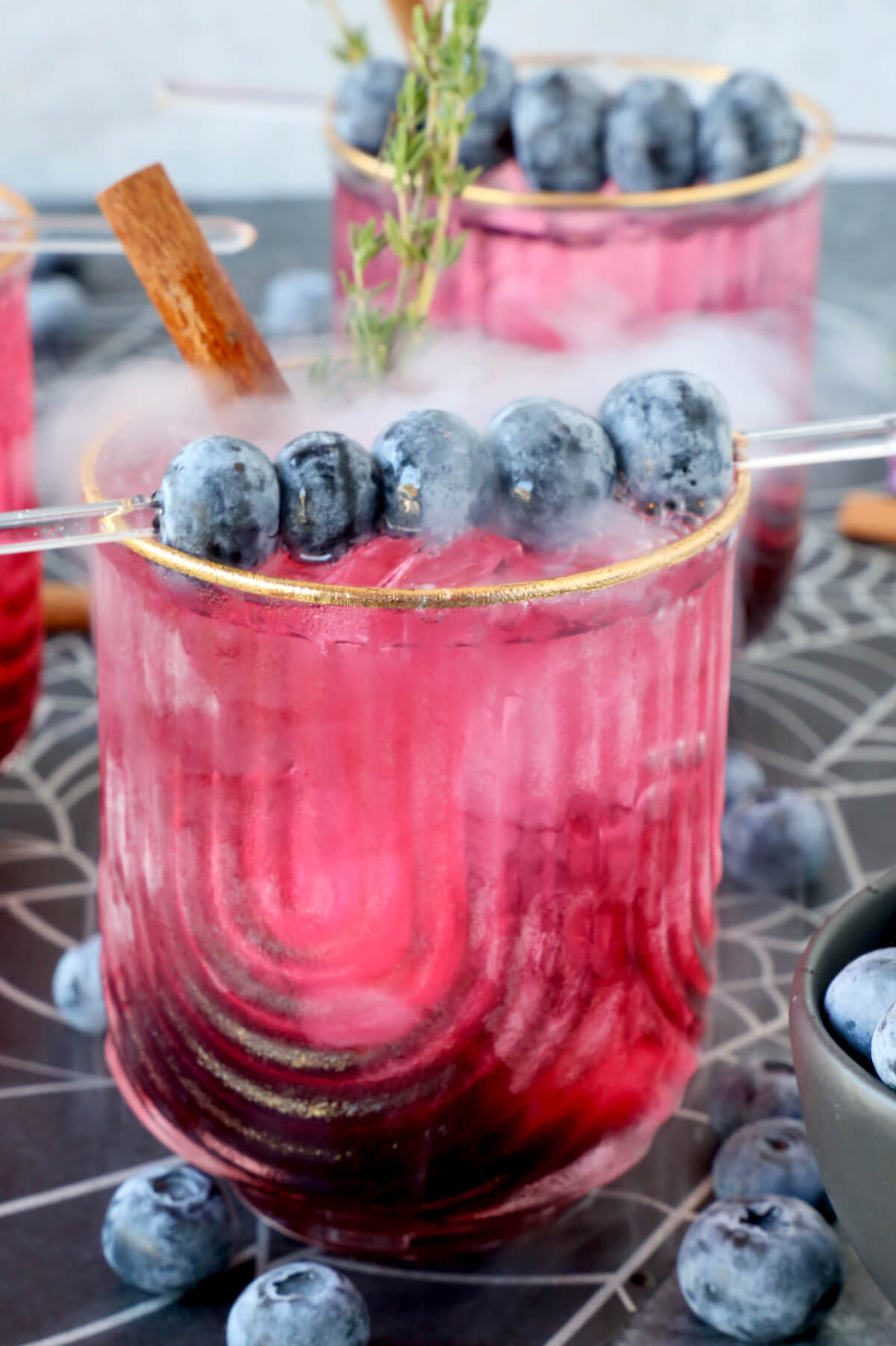 A glass filled with a pink drink with blueberries on top and smoke coming out.  