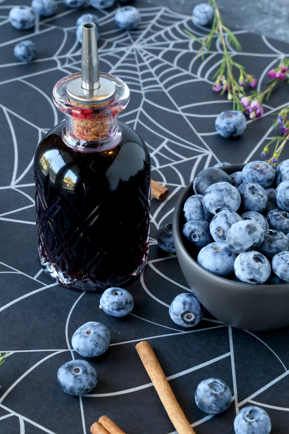 A glass bottle with blueberry syrup next to a bowl of fresh blueberries. 