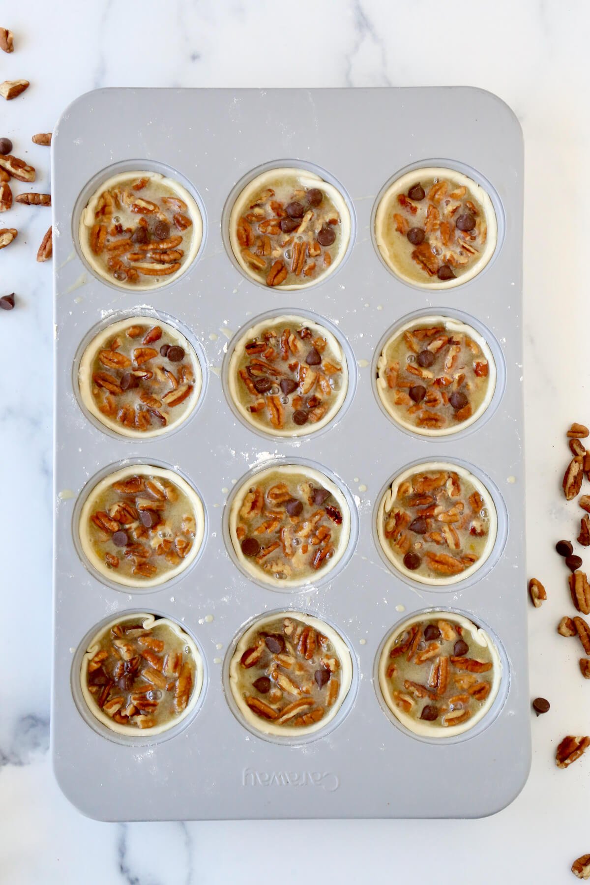 A muffin pan filled with pie dough, chocolate chips, pecans and pecan pie filling.  