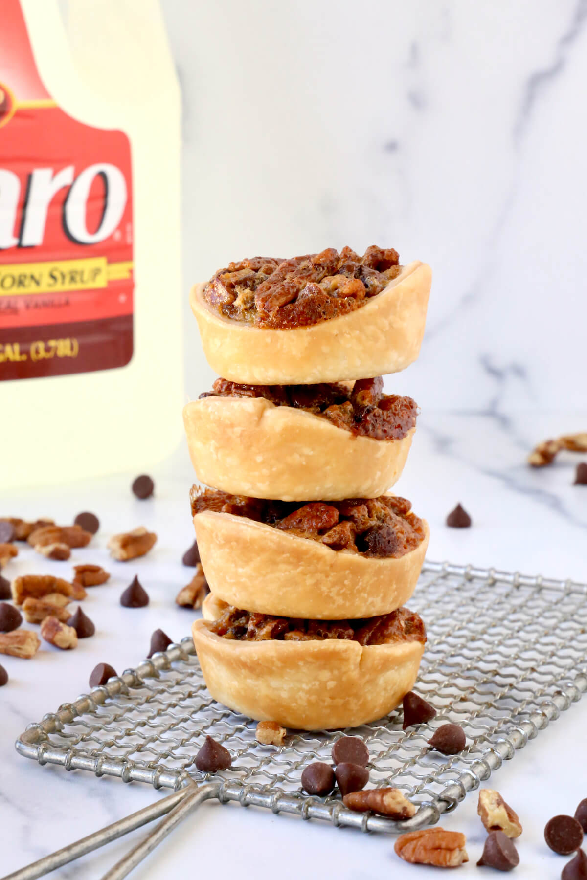 Four pecan tartlets stacked on top of each other in front of a large bottle of corn syrup. 