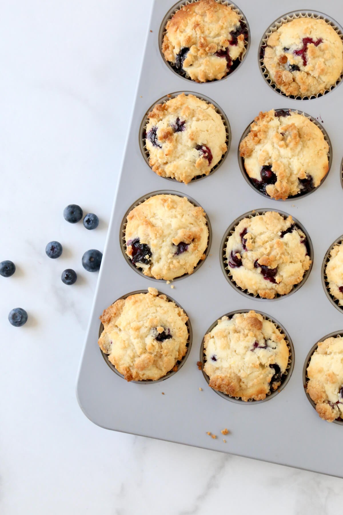 A muffin pan filled with baked muffins and blueberries sitting next to it.  