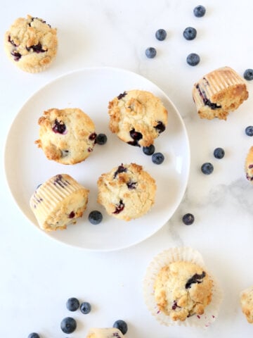 A white plate with blueberry muffins and fresh blueberries.