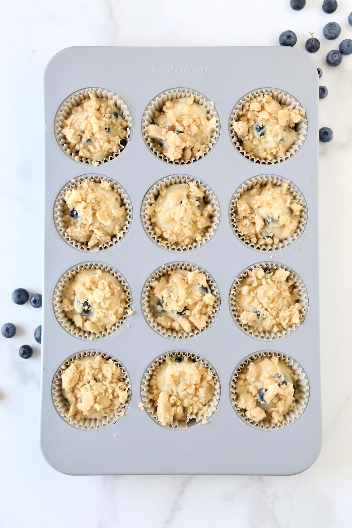 A muffin pan filled with batter and topped with crumble topping.  