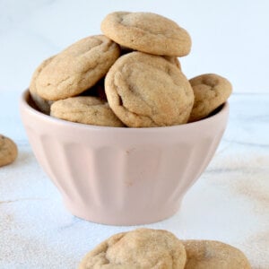 A pink bowl filled with small round cookies and two cookies sitting in the front.