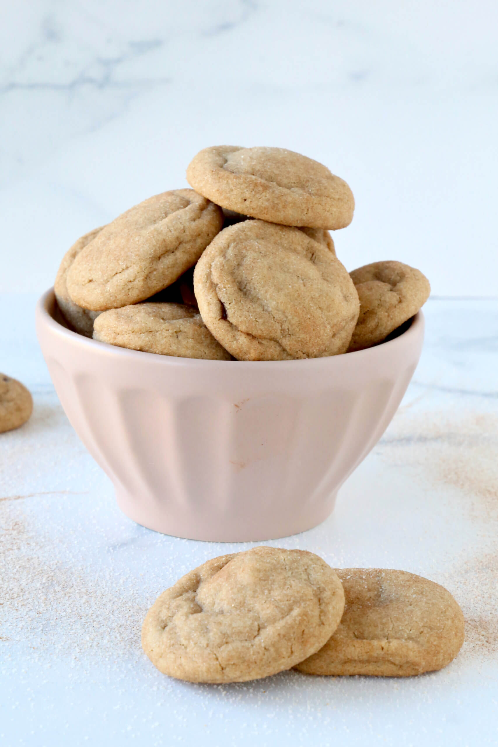 A pink bowl filled with small round cookies and two cookies sitting in the front.