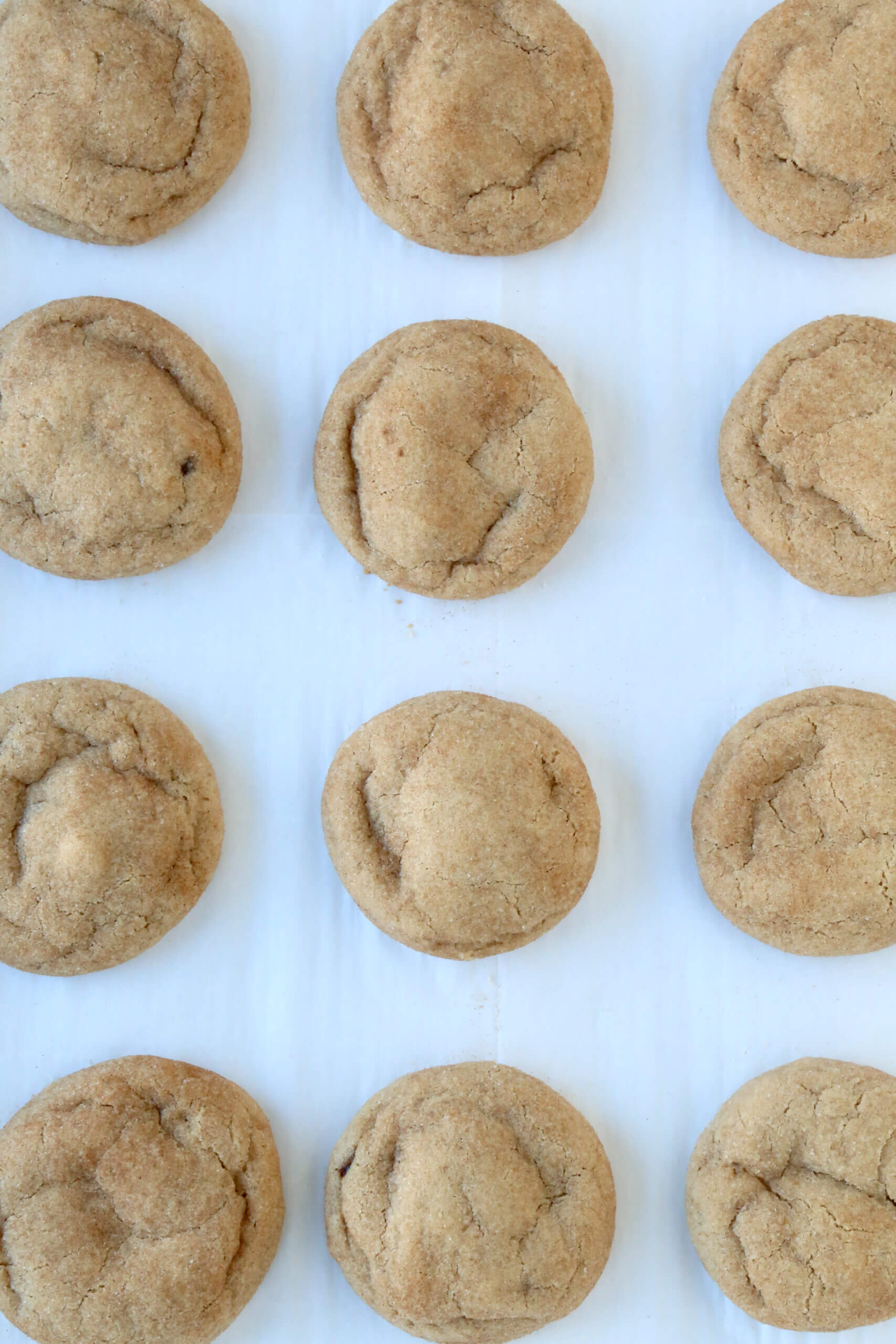 Twelve light brown cookies lined on a sheet pan.
