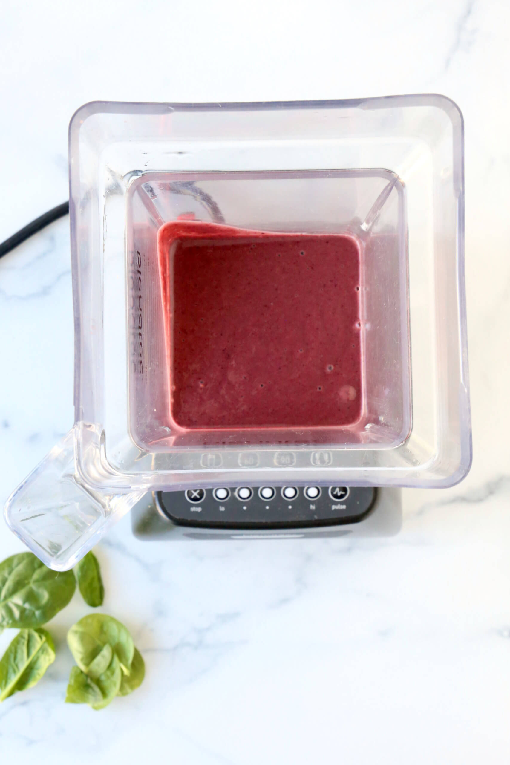 A blender filled with spinach, banana, berries, protein powder.