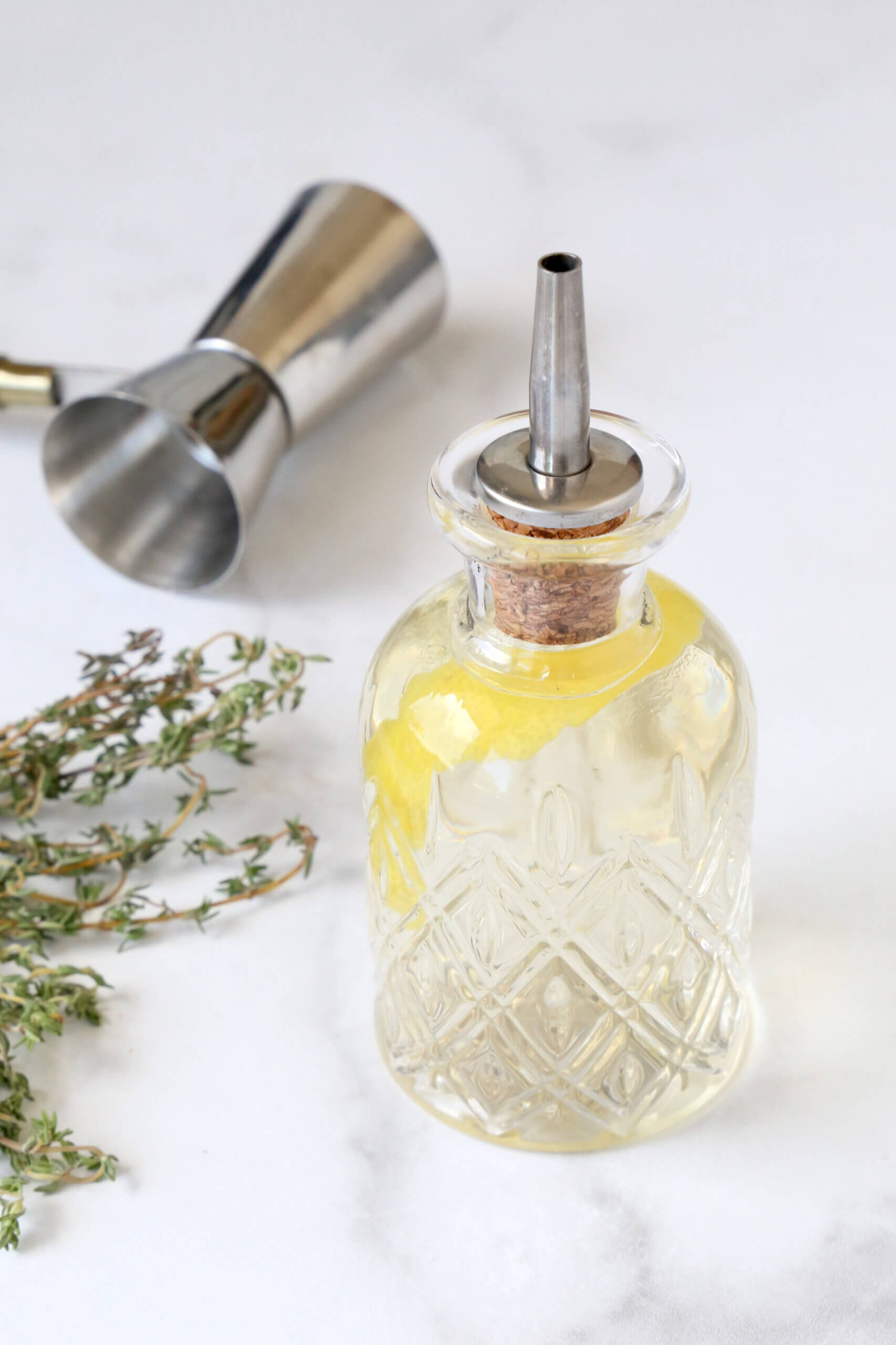 A crystal cut glass jar with a spout, filled with a liquid and a lemon peel.  