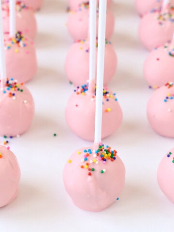 Rows of small pink balls with white stick in it and rainbow sprinkles on top.