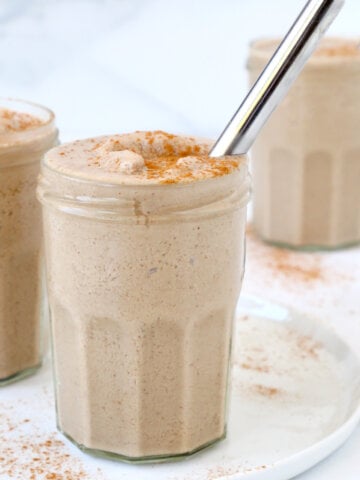 Three drink glasses filled with a light brown smoothie, cinnamon dussted on top and a silver straw.