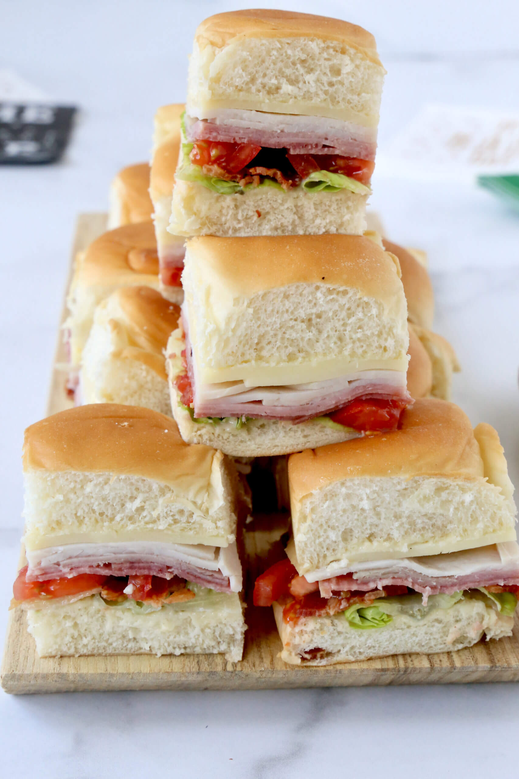 A stack of square sandwiches on a wood board.