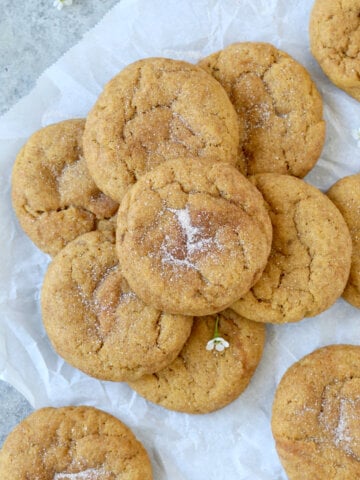 A white piece of parchment paper with eleven round light brown cookies stacked on top.