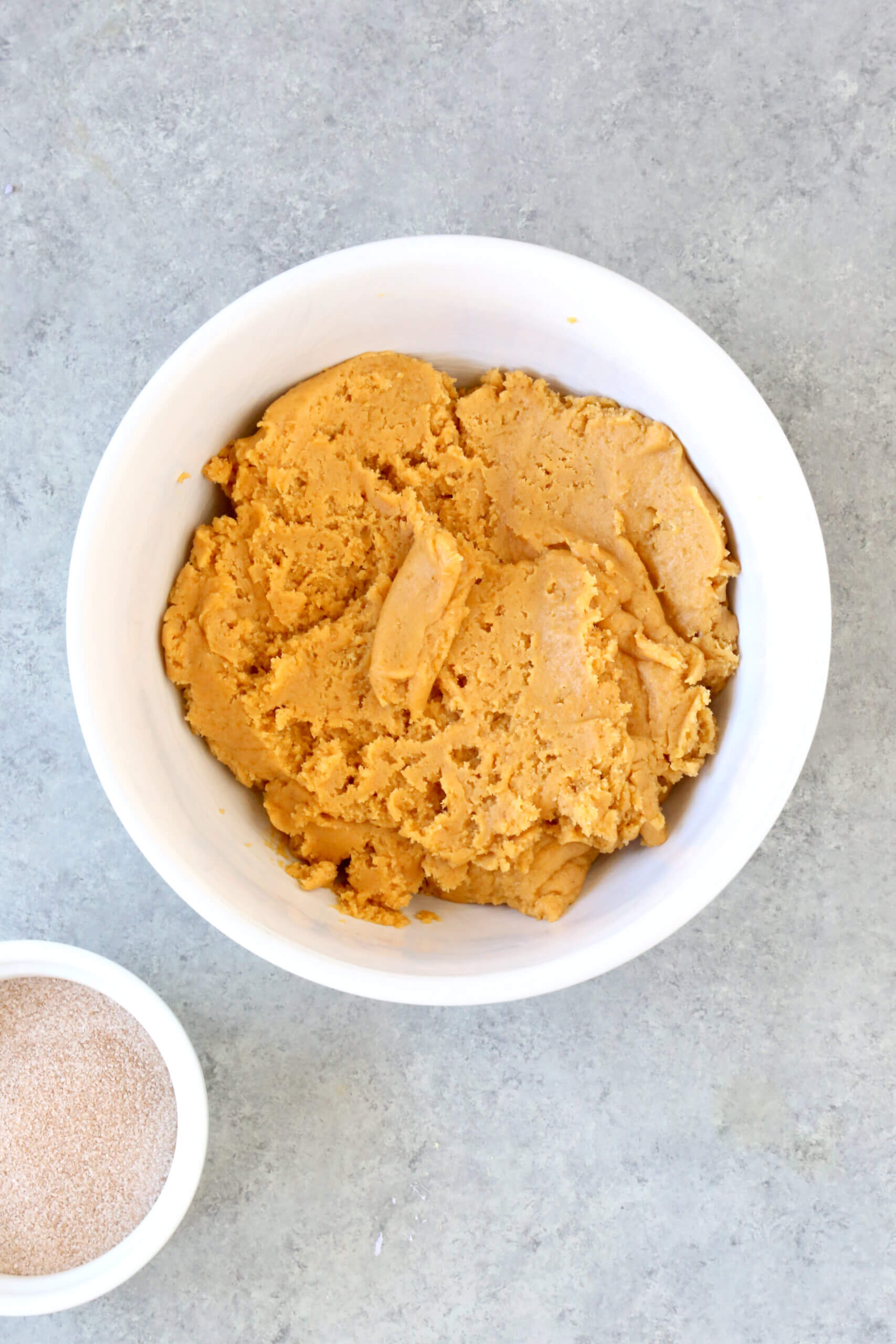 A white bowl filled with orange colored cookie dough. 