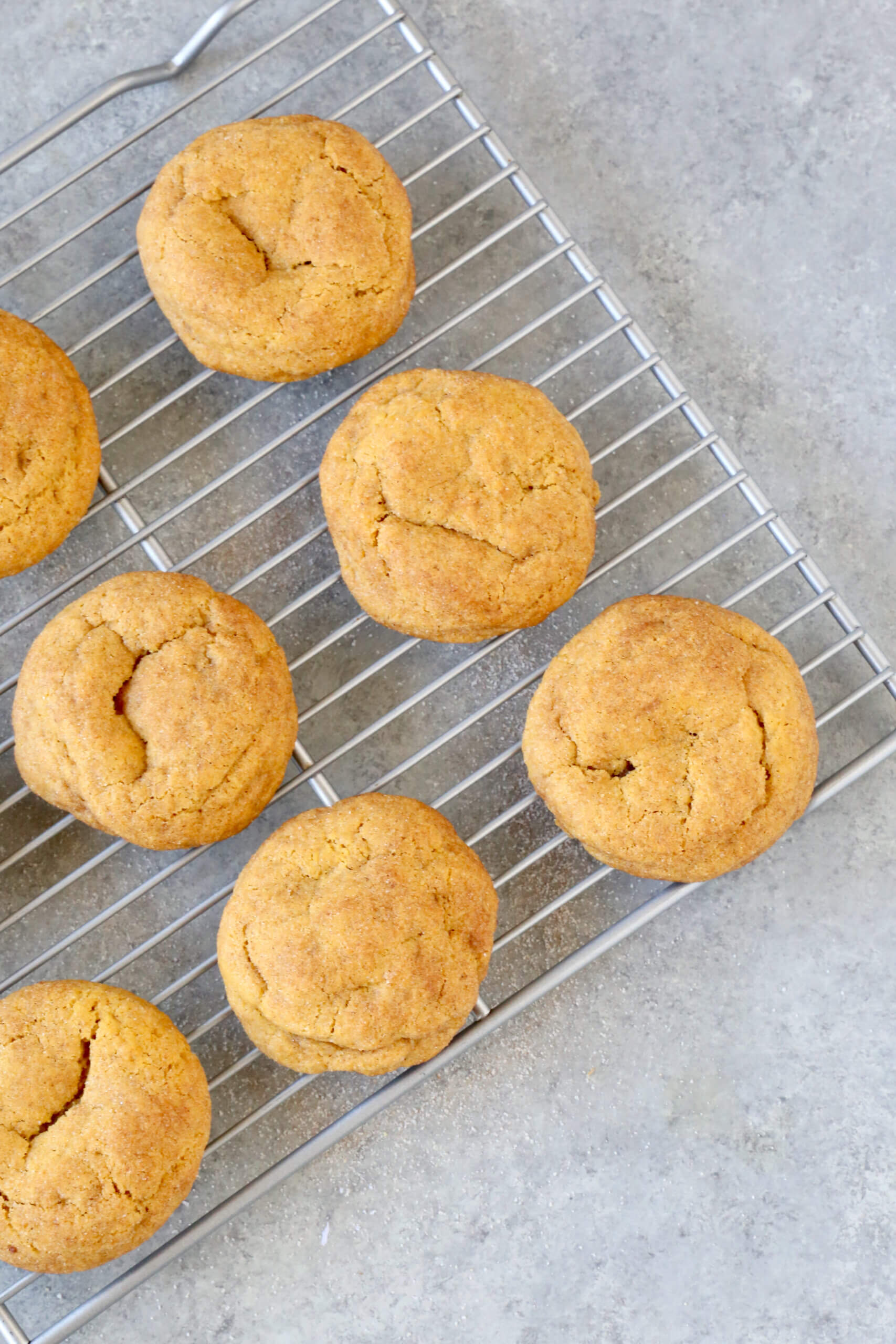 A silver wire cooling rack under light orange colored cookies. 