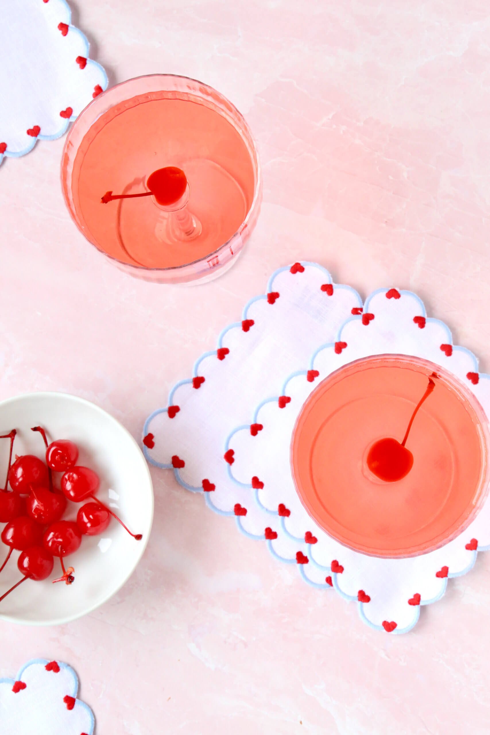 Two glass filled with bright red liquid and a ruby red cherry in each.  