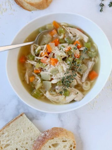 A white bowl filled with a yellow liquid and orange carrots, white chicken, green celery and topped with melted cheese.