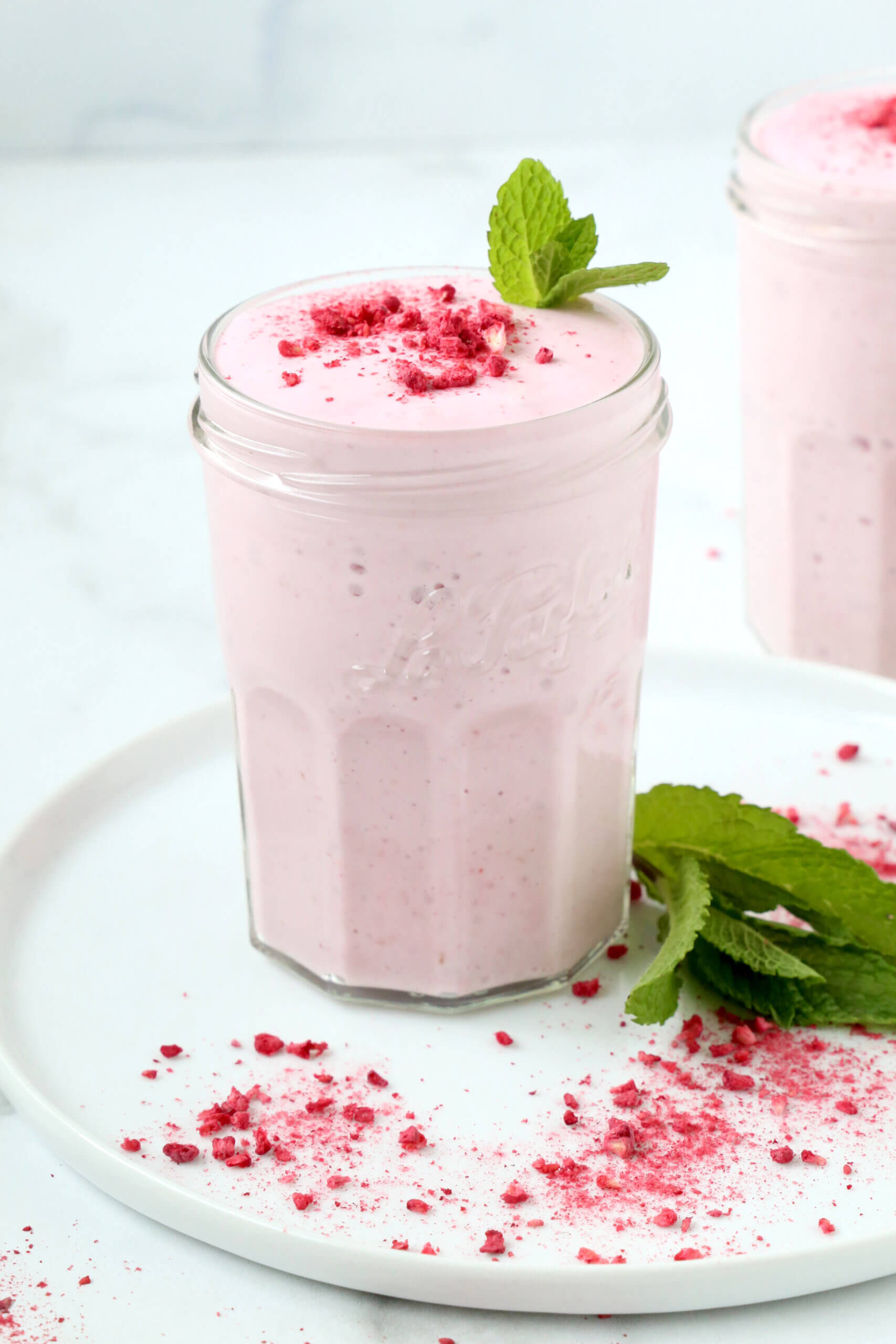 A clear glass filled with a pink creamy liquid, topped with a dark pink powder and a green mint leaf.  