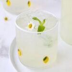 A white plate under three clear glasses with lemons on them, filled with light yellow liquid and green fresh mint leaves.