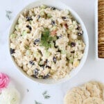 A white bowl filled with chopped chicken salad next to a white box filled with crackers.