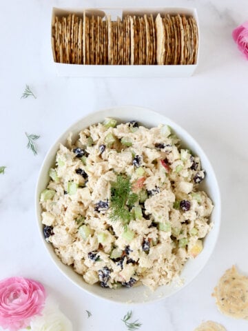 A white bowl filled with chopped chicken salad next to a white box filled with crackers.