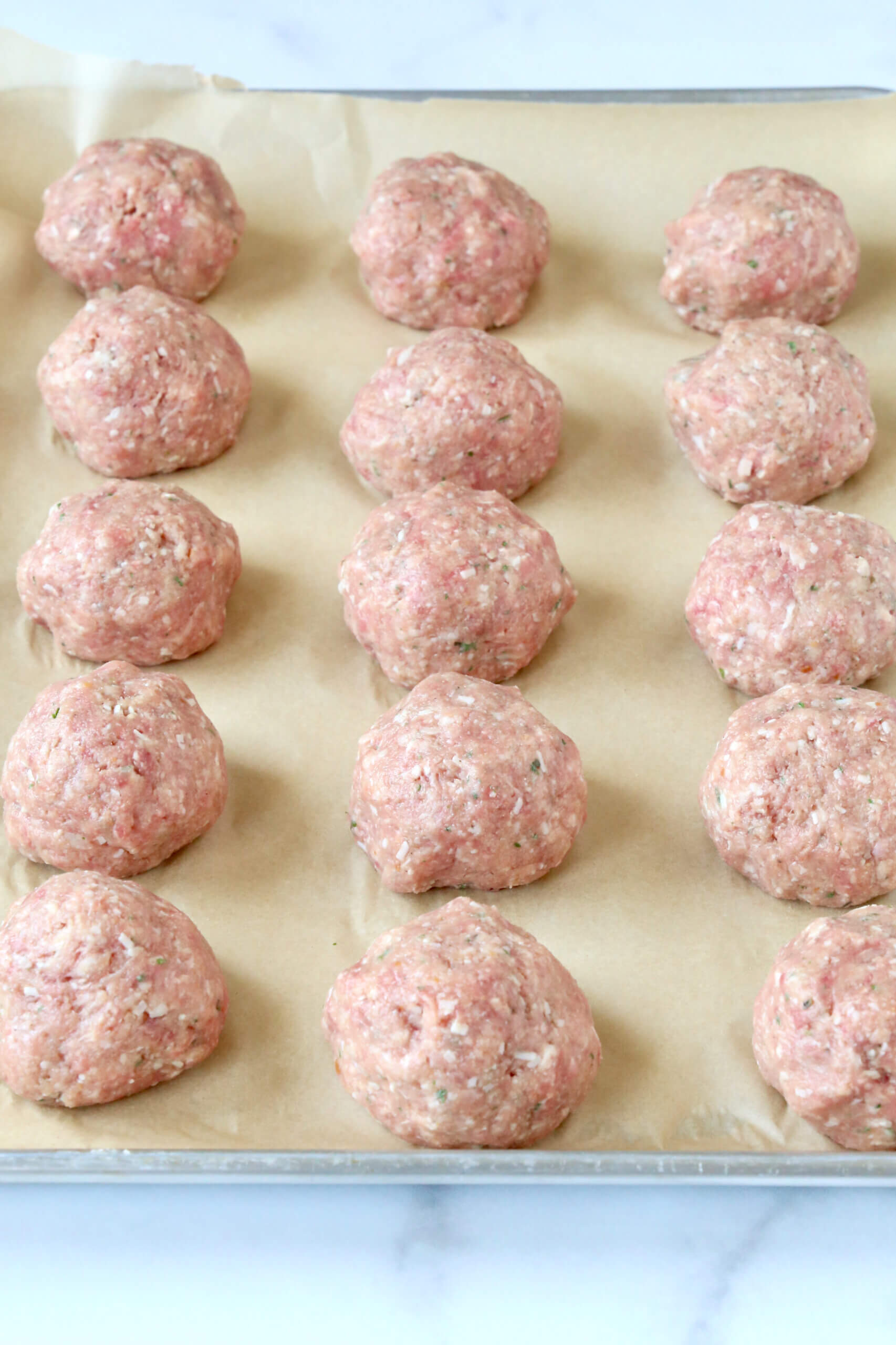 A silver tray lined with light brown paper and fifteen light pink raw balls of meat.