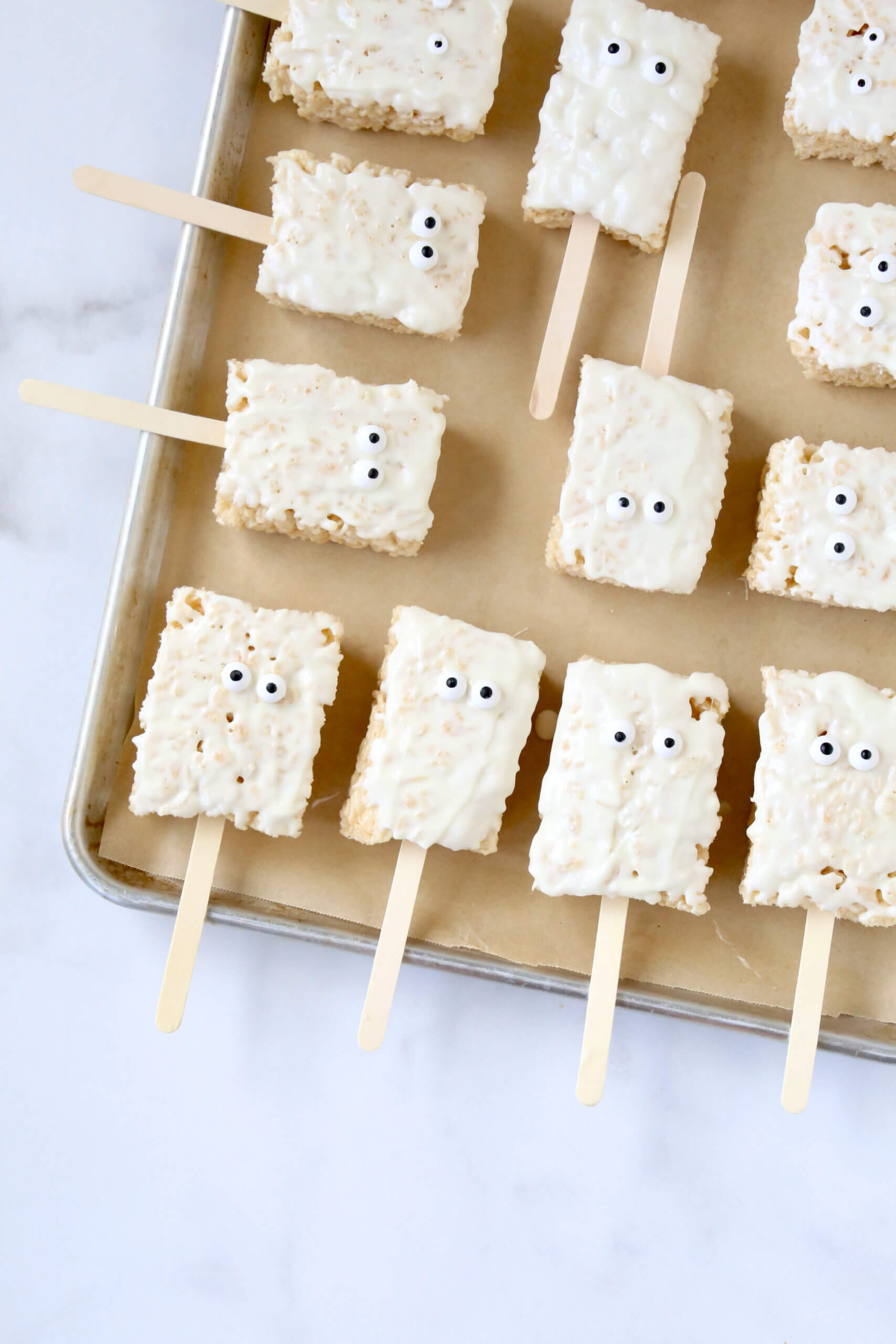 A gold tray with small rectangle rice krispie treats with light brown stick and white chocolate on top.