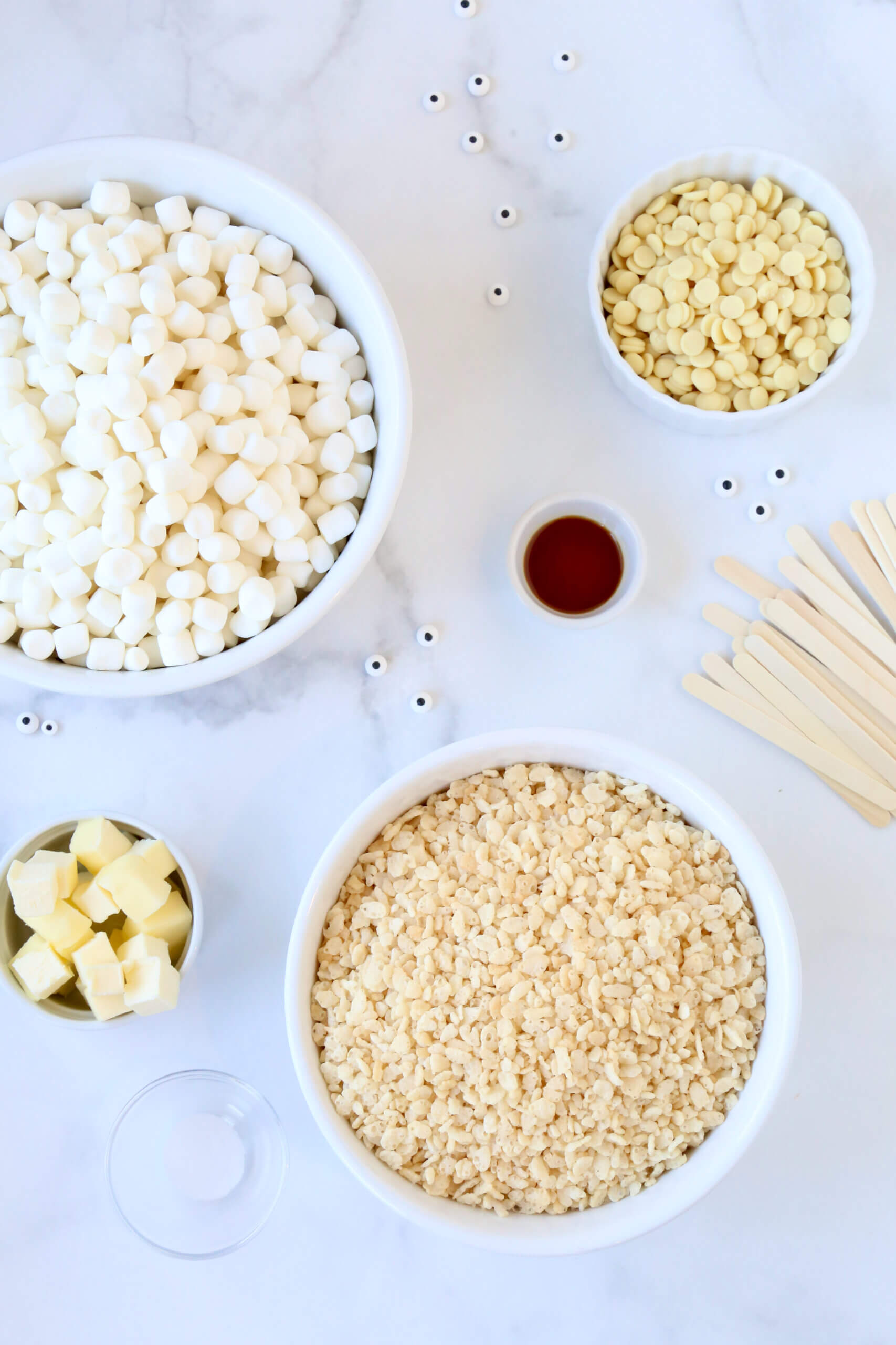 Five bowls filled with marshmallows, rice krispie cereal, white chocolate chips and cubed butter.