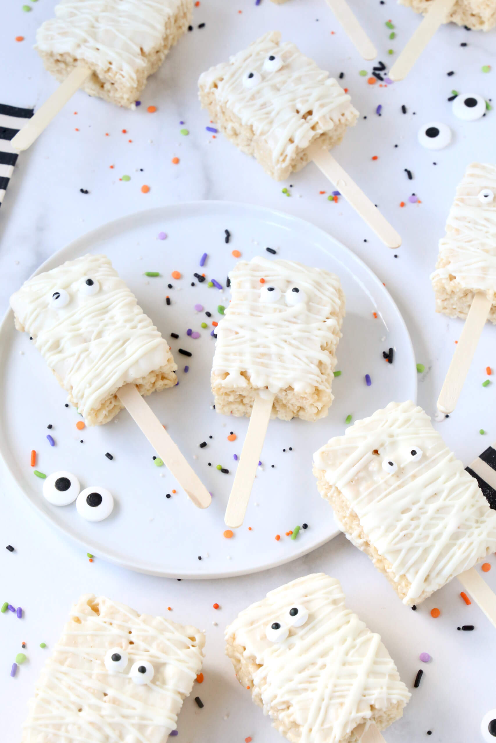 Ten small rectangle rice krispie treats, dipped in white chocolate, next to black and white stripe napkins.