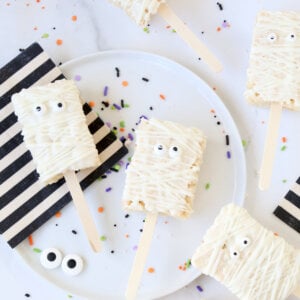 Ten small rectangle rice krispie treats, dipped in white chocolate, next to black and white stripe napkins.
