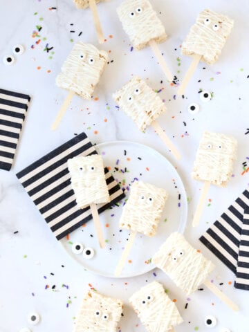 Ten small rectangle rice krispie treats, dipped in white chocolate, next to black and white stripe napkins.