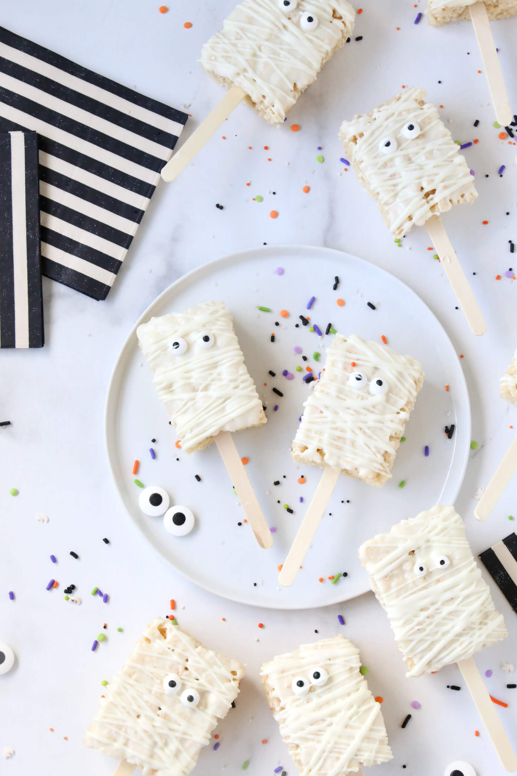 Ten small rectangle rice krispie treats, dipped in white chocolate, next to black and white stripe napkins.