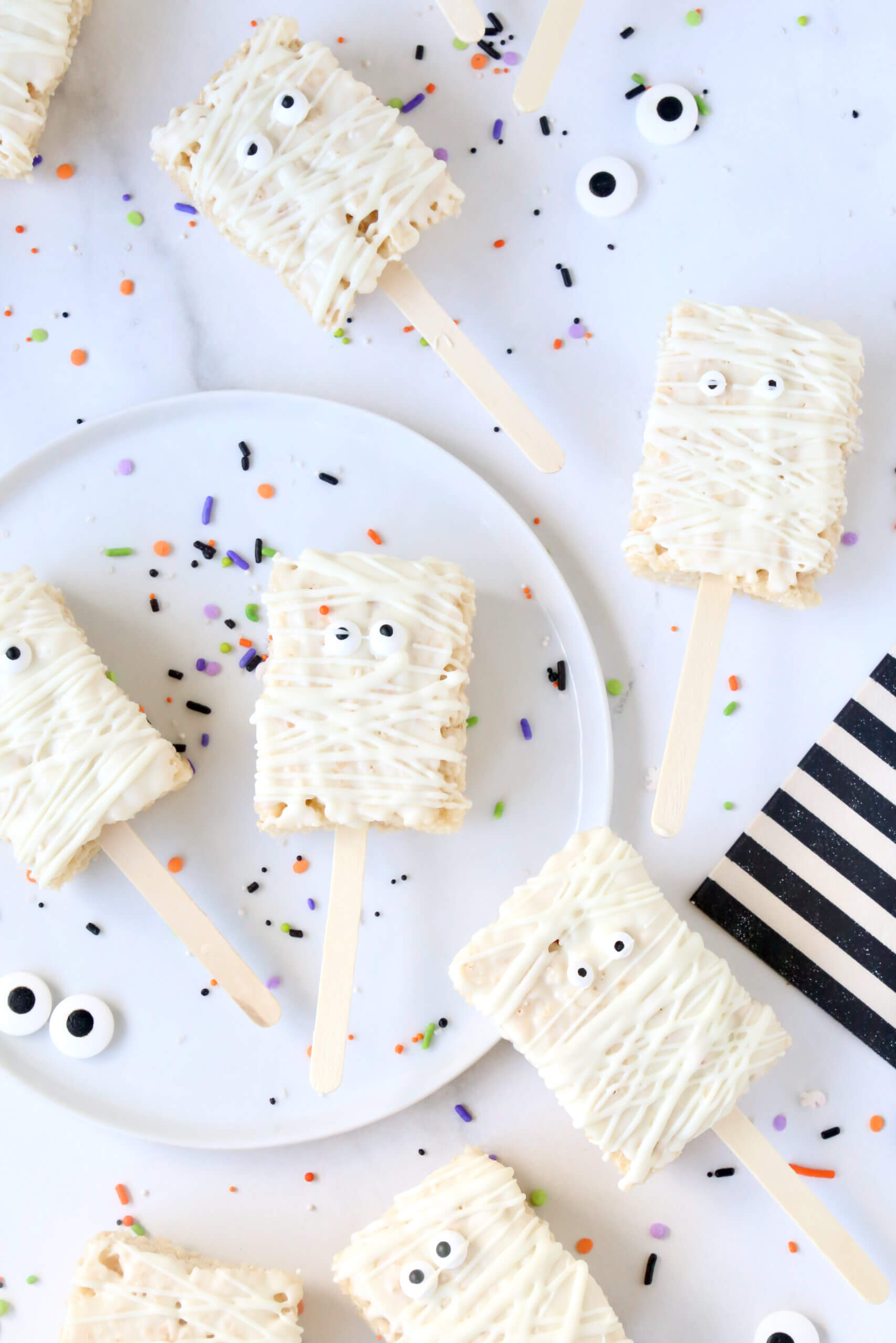 Ten small rectangle rice krispie treats, dipped in white chocolate, next to black and white stripe napkins.