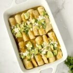 Easy chicken avocado enchiladas in a baking dish topped with tomatillo sauce, cotija cheese and fresh cilantro.