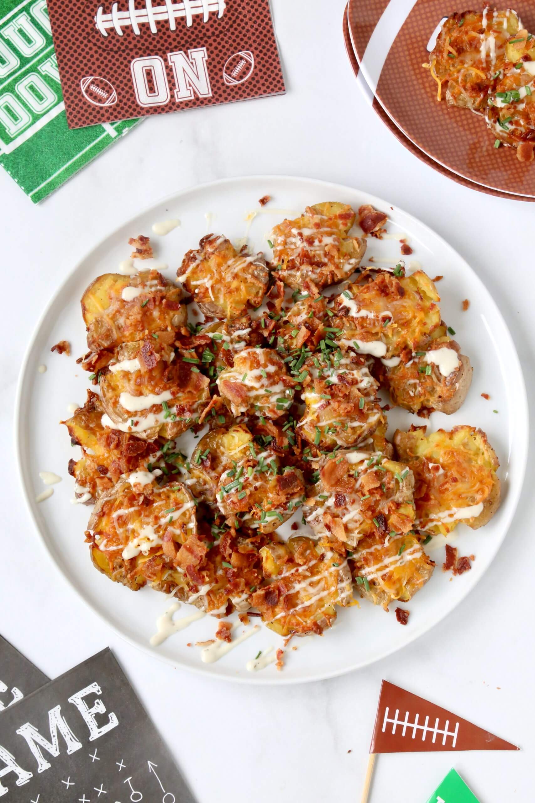 A white plate filled with light brown smashed potatoes topped with crumbled bacon, green chives and yellow cheese.