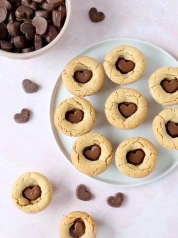 A white plate filled with light brown peanut butter cookies with chocolate hearts in the center.