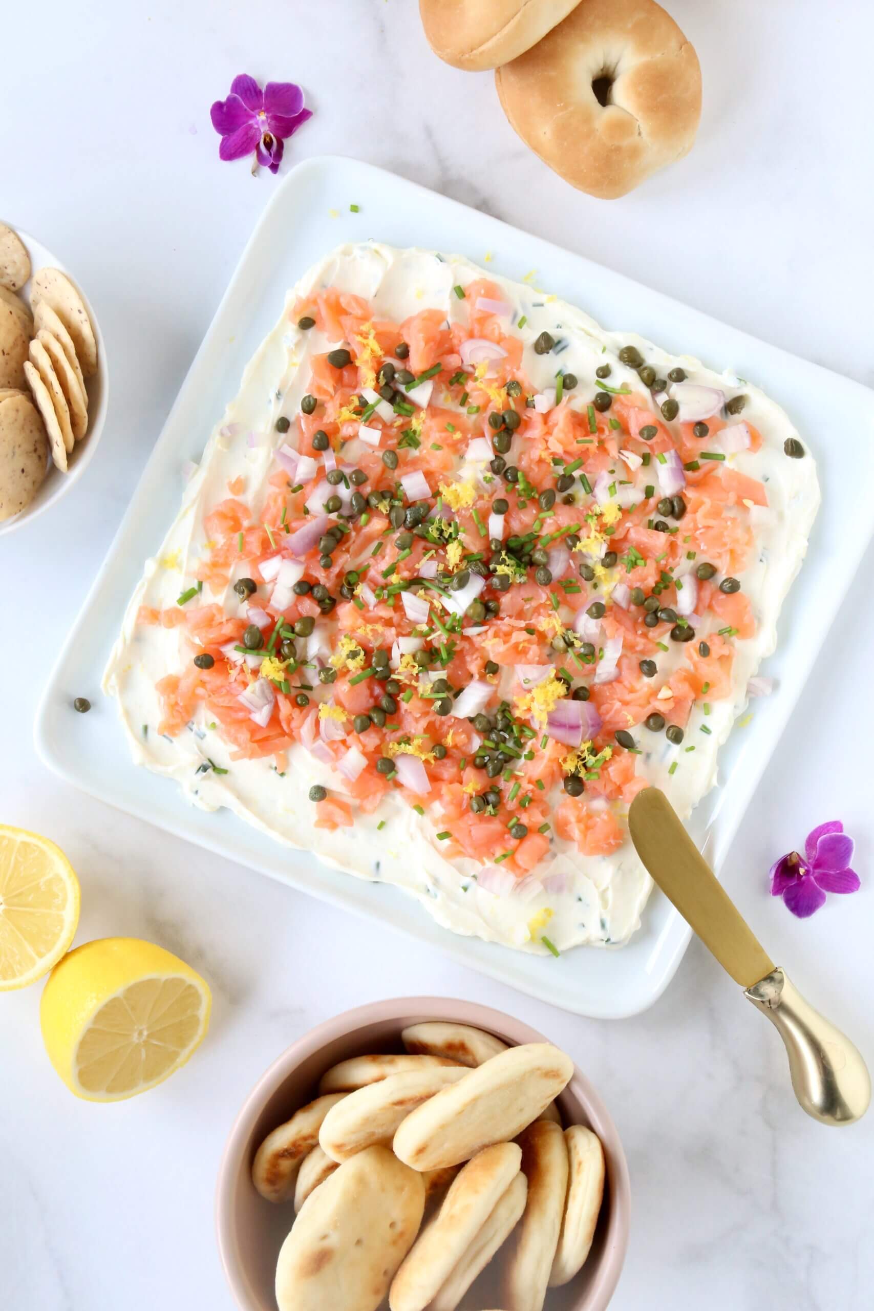 A white platter with a white cream cheese spread and orange smoke salmon on top.