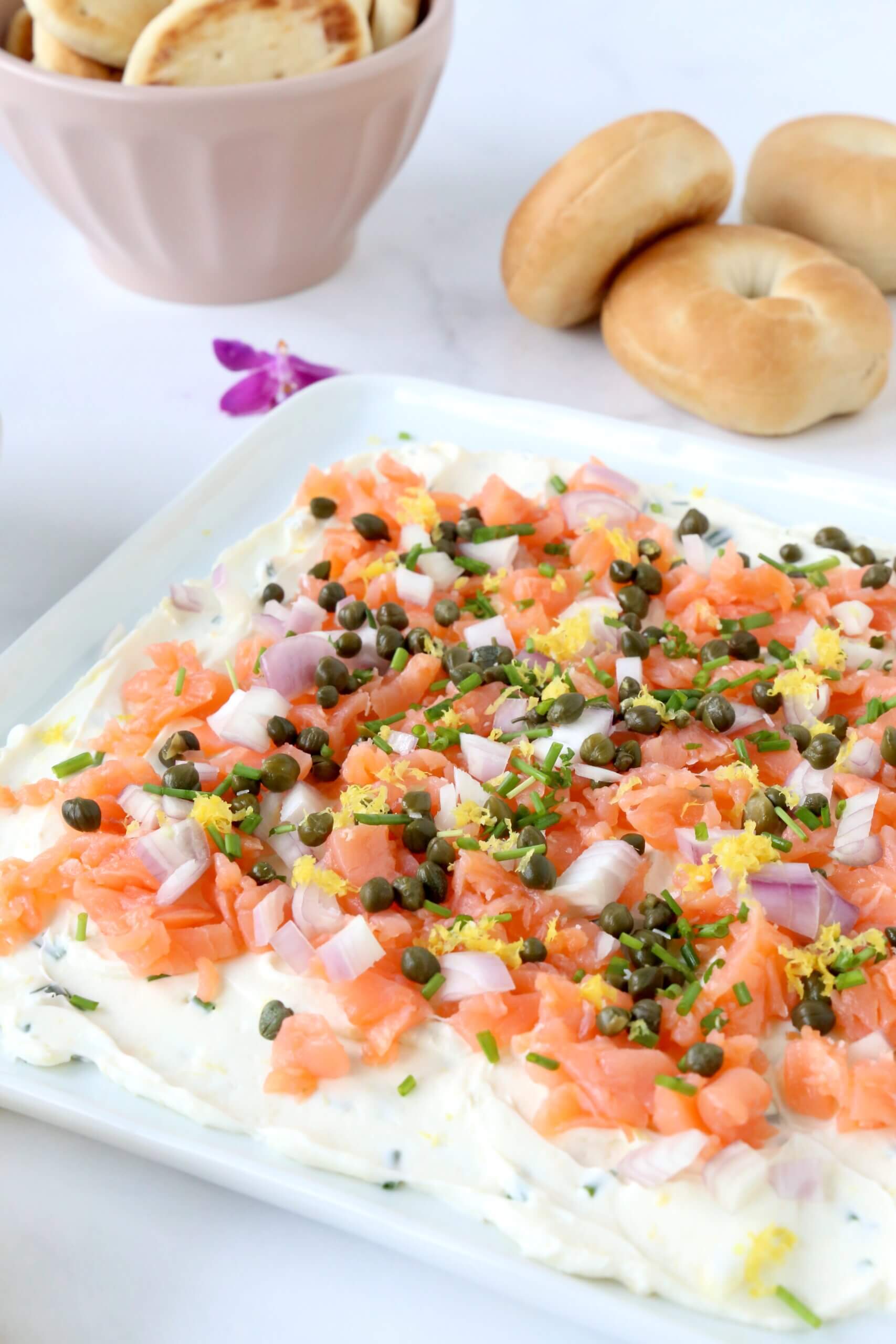 A white platter with a white cream cheese spread and orange smoke salmon on top.