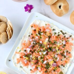 A white platter with a white cream cheese spread and orange smoke salmon on top.
