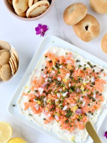 A white platter with a white cream cheese spread and orange smoke salmon on top.