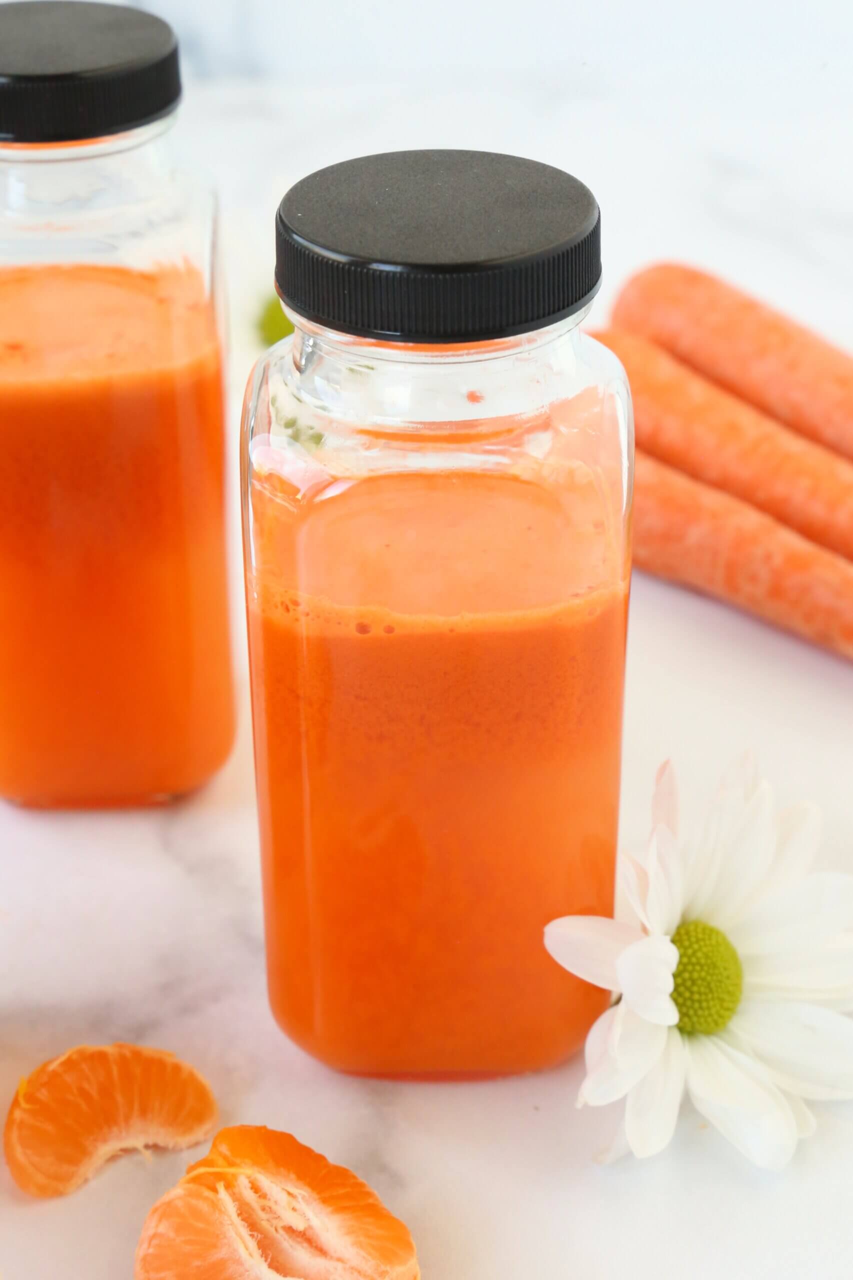 Three glass bottles with a black lid that is filled with orange carrot juice.